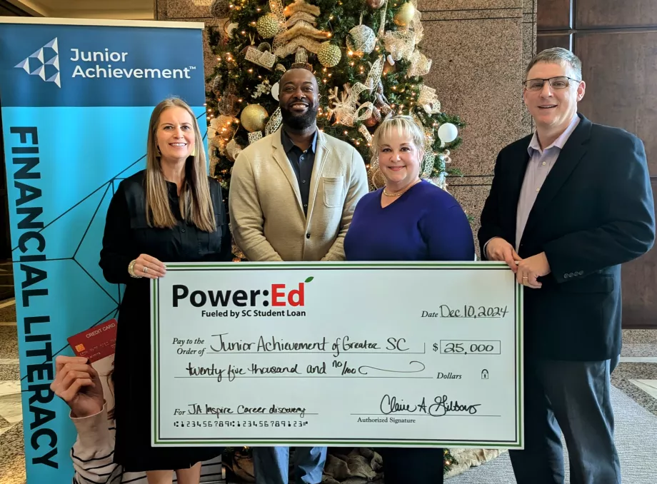 Executives pose with ceremonial check in front of Christmas tree