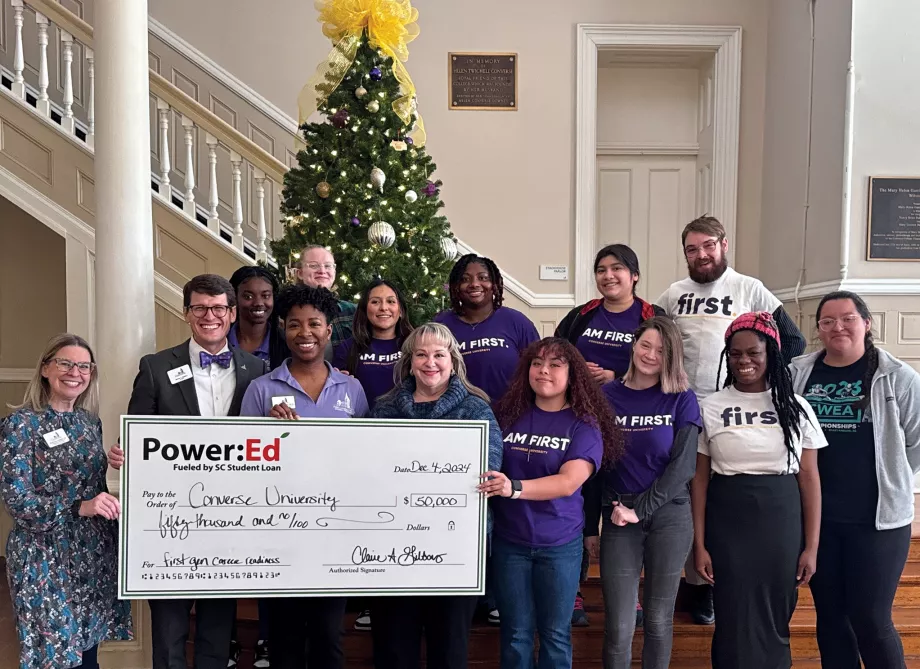 Students and adults pose with big ceremonial check in front of Christmas tree