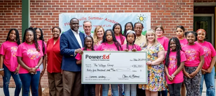 Adults and girls pose with ceremonial check